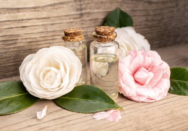Camellia oil bottles and camellia flowers on rustic wooden table
