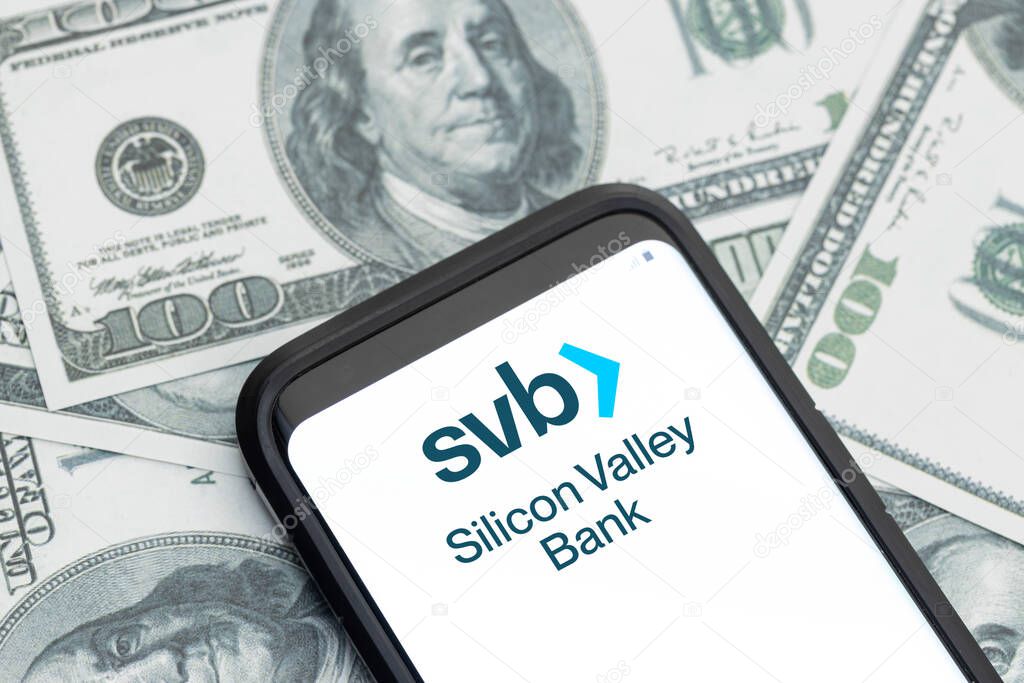 Galicia, Spain; march 12, 2023: Silicon Valley Bank financial services company logo on Smartphone screen and dollar banknotes background