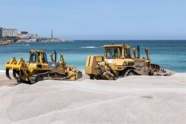 Coruna, İspanya; 18 Mayıs 2023: Coruna şehrinin Riazor plajına kum saçmaya çalışan iki buldozer sahnesi