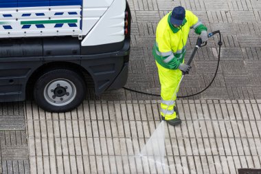 Yüksek basınçlı su jeti makinesiyle kaldırımı temizleyen bir işçi. Şehir temizlik ve bakım hizmetleri