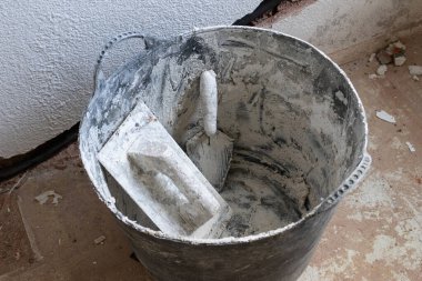 Mallar ve diğer aletler bir inşaat sahasında bir kovanın içinde, bir ev yenileme projesi sırasında toz ve molozla kaplı bir şekilde duruyor.