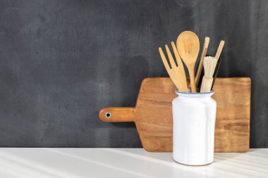 Beyaz seramik kabın içindeki ahşap mutfak gereçleri ve tahta kesme tahtası fotokopi alanı ile karatahta duvara yaslanarak rahat bir mutfak sahnesi yaratıyor.