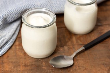 Yoğurt kavanozları, ahşap masa, kaşık ve mavi kumaşla dolu sakin bir hayat.