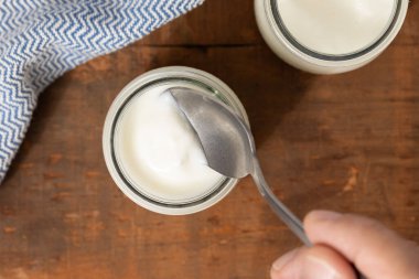 Kremalı yoğurt, cam bir kavanozdan kaşıkla çıkarılıyor, kırsal ahşap bir masada, üst görünümde.