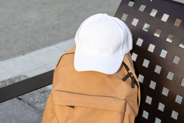 Kentsel bir sırt çantasının üstünde boş beyaz bir beyzbol şapkası. Şablon Ayarla