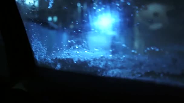 行方不明車の窓 車の窓に雪を溶かす 雪に覆われたガラスの後ろの車のヘッドライト ボケと明るい色の反射 — ストック動画
