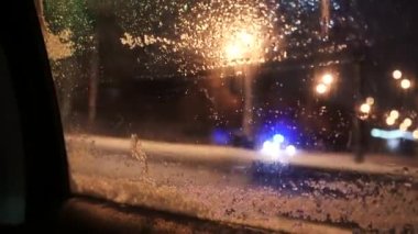 Misted araba penceresi. Arabanın camında eriyen karlar. Araba farları, bokeh ve kar kaplı camların arkasında parlak renkli yansımalar.