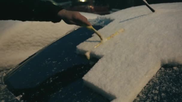 運転する前にアイススクレーパーで雪から車のサイドウィンドウを掃除します 男は車の窓から氷を取り除く 雪の降る冬の夜に車を掃除する男 — ストック動画