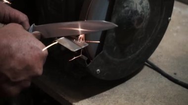 Elektrikli değirmen çarkında bir bıçağı bilemek, makine elektrikli öğütücüde bir kınkanatlıyı bilemek, dönen taşta elle bilemek, yakın plan.