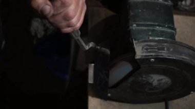 Elektrikli değirmen çarkında bir bıçağı bilemek, makine elektrikli öğütücüde bir kınkanatlıyı bilemek, dönen taşta elle bilemek, yakın plan.