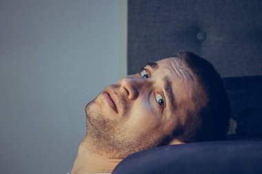 30 'lu ve 40' lı yaşlarda yakışıklı bir adamın dramatik bir hayat tarzı portresi. Üzüntülü bir şekilde yatakta oturuyor ve depresyondan muzdarip. Çekici depresif ve üzgün bir adam.