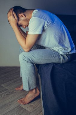 30 'lu ve 40' lı yaşlarda yakışıklı bir adamın dramatik bir hayat tarzı portresi. Üzüntülü bir şekilde yatakta oturuyor ve depresyondan muzdarip. Çekici depresif ve üzgün bir adam.