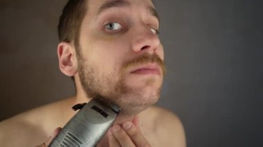 Yüz traş makinesi. Tıraş makinesiyle sakal kes. Sakallı adam tıraş işlemi. Tıraşsız adam. Sakal tıraşı. Tıraş olan adamın yüzünü yakından çek. Adam sakalını kesti. kuru traş makinesi.