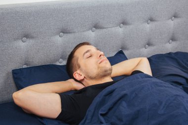 Geceleri yatak odasında, yatakta rahat uyuyan yakışıklı bir delikanlının en iyi görüntüsü. Farklı pozisyonlarda uyu. Bekar odası. Derin uyku.