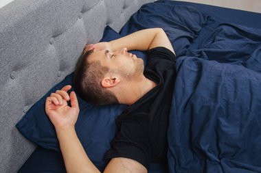 Geceleri yatak odasında, yatakta rahat uyuyan yakışıklı bir delikanlının en iyi görüntüsü. Farklı pozisyonlarda uyu. Bekar odası. Derin uyku.