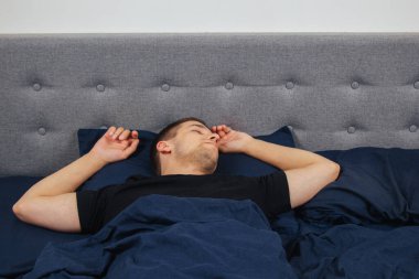 Geceleri yatak odasında, yatakta rahat uyuyan yakışıklı bir delikanlının en iyi görüntüsü. Farklı pozisyonlarda uyu. Bekar odası. Derin uyku.