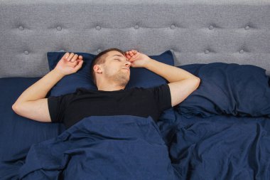 Geceleri yatak odasında, yatakta rahat uyuyan yakışıklı bir delikanlının en iyi görüntüsü. Farklı pozisyonlarda uyu. Bekar odası. Derin uyku.