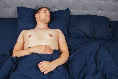 Yakışıklı genç adam geceleri yatak odasında rahat bir şekilde uyuyor. Elbiseleri olmadan. Bekar odası. Derin uyku.