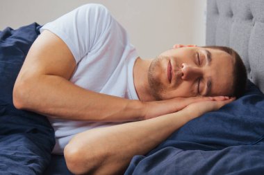 Geceleri yatak odasında, yatakta rahat uyuyan yakışıklı bir delikanlının en iyi görüntüsü. Farklı pozisyonlarda uyu. Bekar odası. Derin uyku.