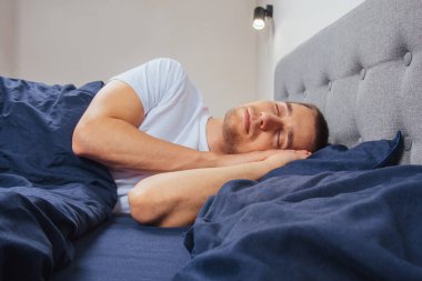 Top view of a handsome young man sleeping comfortably on the bed at night in his bedroom. Sleep in different positions. Bachelor bedroom. Deep sleep clipart