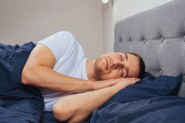 Geceleri yatak odasında, yatakta rahat uyuyan yakışıklı bir delikanlının en iyi görüntüsü. Farklı pozisyonlarda uyu. Bekar odası. Derin uyku.