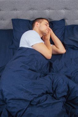 Geceleri yatak odasında, yatakta rahat uyuyan yakışıklı bir delikanlının en iyi görüntüsü. Farklı pozisyonlarda uyu. Bekar odası. Derin uyku.