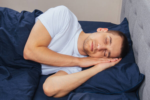 Top view of a handsome young man sleeping comfortably on the bed at night in his bedroom. Sleep in different positions. Bachelor bedroom. Deep sleep