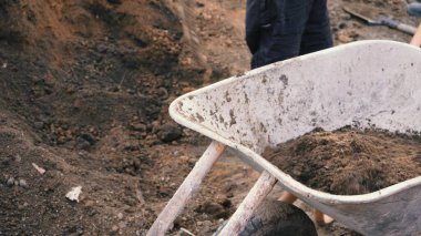 Bir işçi el arabasına kürekle 4K 'lık toprak döker. Trolley toprak dolu. Ev yapımı el yapımı bir alet..