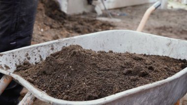 Bir işçi el arabasına kürekle 4K 'lık toprak döker. Trolley toprak dolu. Ev yapımı el yapımı bir alet..