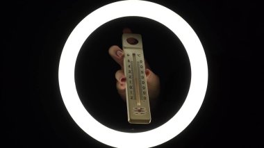 plastic alcohol thermometer with a red stripe in female hands close-up on a black background. temperature measurement concept.