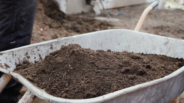 Bir işçi el arabasına kürekle 4K 'lık toprak döker. Trolley toprak dolu. Ev yapımı el yapımı bir alet..