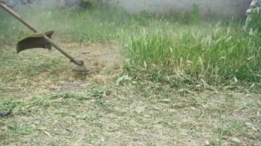 Yeşil kot pantolonlu erkek bacaklarının, yeşil çim biçen bir biçme makinesinin arka planına yakın plan çekimi. Çimleri elle biçme makinesiyle biçmek. Bahçe ve çim bakımı