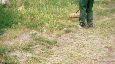 Yeşil kot pantolonlu erkek bacaklarının, yeşil çim biçen bir biçme makinesinin arka planına yakın plan çekimi. Çimleri elle biçme makinesiyle biçmek. Bahçe ve çim bakımı