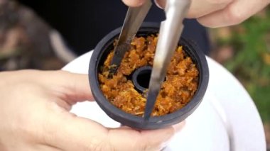 Mens hands clog tobacco into a hookah bowl. Smoking in nature. Relaxation, rest. Smoking is harmful to health. The process of preparing for smoking a hookah