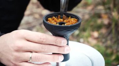 Mens hands clog tobacco into a hookah bowl. Smoking in nature. Relaxation, rest. Smoking is harmful to health. The process of preparing for smoking a hookah