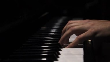 Piano keys close up in dark colors. Student trains to play the piano. Man two hands plays gentle classical music on a beautiful grand piano in a classroom close up