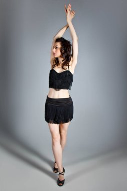 Beautiful young woman with evening make-up and hairdo dancing in elegant black dress with passion. Studio portrait on a gray background. Dancing, tango style