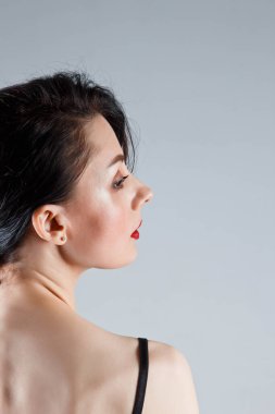 beautiful young brunette girl with a bare back on a gray background. the concept of femininity and tenderness. cosmetology