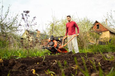 Planting vegetables under the walk-behind tractor. A man with a walk-behind tractor in the garden. Manual work with equipment. An elderly man teaches a young boy to plow the land