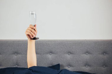Yatakta bir adamın elinde şampanya. Akşamdan kalma, alkol zehirlenmesi konsepti. Tatil selamları.