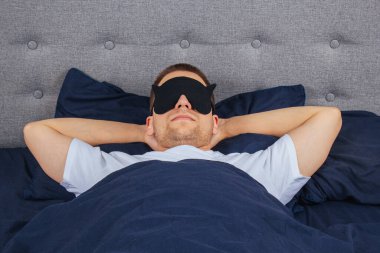 Yüksek açılı fotoğraf, uyku maskesi takan genç adam mutlu bir gülümseme, uyku battaniyesi, battaniye, elbiseler, pijamalar.