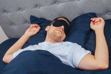 Yüksek açılı fotoğraf, uyku maskesi takan genç adam mutlu bir gülümseme, uyku battaniyesi, battaniye, elbiseler, pijamalar.