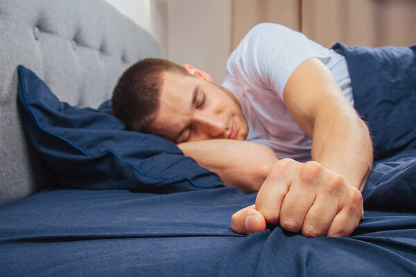 Сонный молодой человек протягивает руку, чтобы отключить сигнализацию. селективный фокус