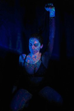 A beautiful young girl with makeup from ultraviolet paints smokes. Releases smoke from the mouth. Holiday of colors holly. Bright, colorful, festive coloring book. Fluorescent makeup on the face