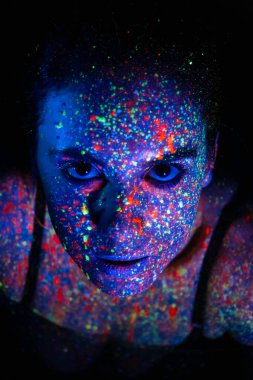 Beautiful young sexy girl dances with paint on television. Girl with neon body art in colored light