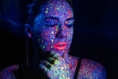 Fashion model woman in neon light, portrait of a beautiful model with fluorescent makeup, body art design in UV, painted face, colorful makeup, on a black background of a girl. Disco dancer in neon light