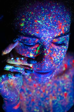 Fashion model woman in neon light, portrait of a beautiful model with fluorescent makeup, artistic design of disco dancers posing in UV, colorful makeup. Isolated on black background