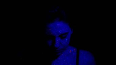 Güzel genç seksi kız televizyonda boyayla dans ediyor. Renkli ışık saçan neon vücutlu bir kız.