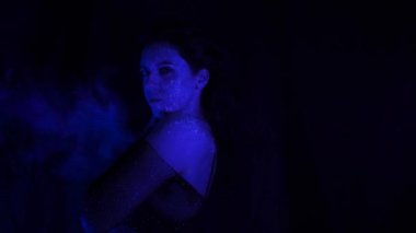 A beautiful young girl with makeup from ultraviolet paints smokes. Releases smoke from the mouth. Holiday of colors holly. Bright, colorful, festive coloring book. Fluorescent makeup on the face