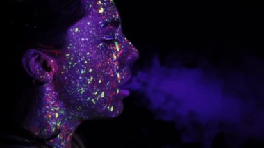 A beautiful young girl with makeup from ultraviolet paints smokes. Releases smoke from the mouth. Holiday of colors holly. Bright, colorful, festive coloring book. Fluorescent makeup on the face